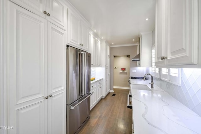 kitchen featuring wall chimney range hood, backsplash, light stone countertops, white cabinets, and high end refrigerator