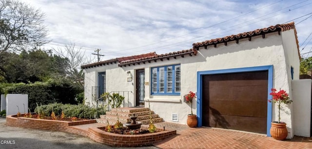 view of front of property with a garage, a tiled roof, decorative driveway, and stucco siding