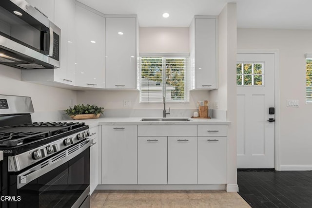 kitchen with stainless steel appliances, sink, wood-type flooring, and white cabinets