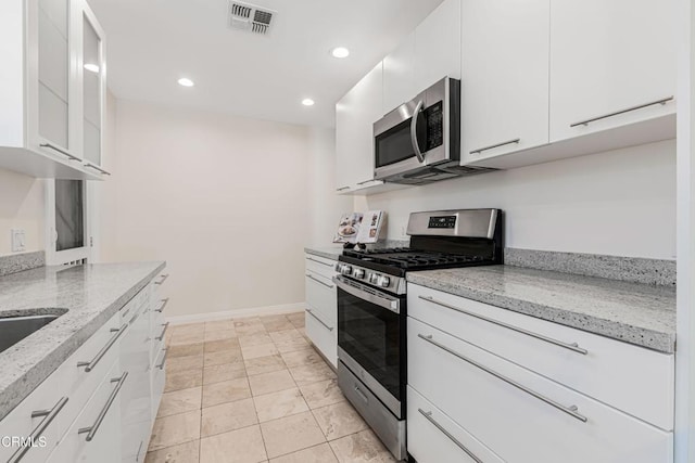 kitchen with stainless steel appliances, white cabinetry, and light stone countertops