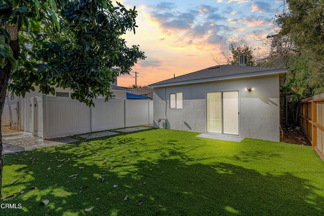 back house at dusk featuring a lawn