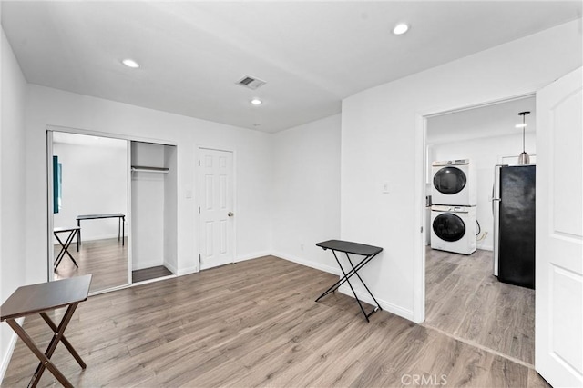 laundry area with hardwood / wood-style floors and stacked washer and clothes dryer