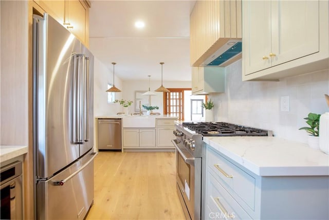 kitchen featuring hanging light fixtures, high end appliances, custom exhaust hood, light hardwood / wood-style floors, and light stone countertops