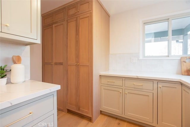 kitchen featuring light stone counters, decorative backsplash, and light wood-type flooring