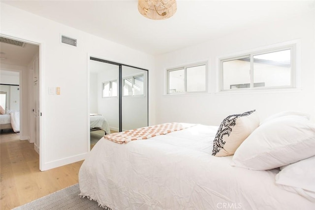 bedroom with light wood finished floors, baseboards, visible vents, and a closet