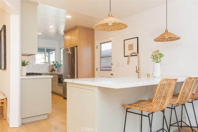 kitchen with a kitchen breakfast bar, light hardwood / wood-style floors, high quality fridge, light brown cabinetry, and kitchen peninsula