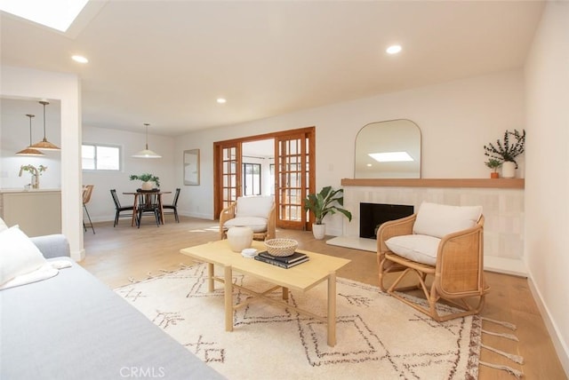 living area with a skylight, french doors, light wood finished floors, recessed lighting, and a fireplace with raised hearth