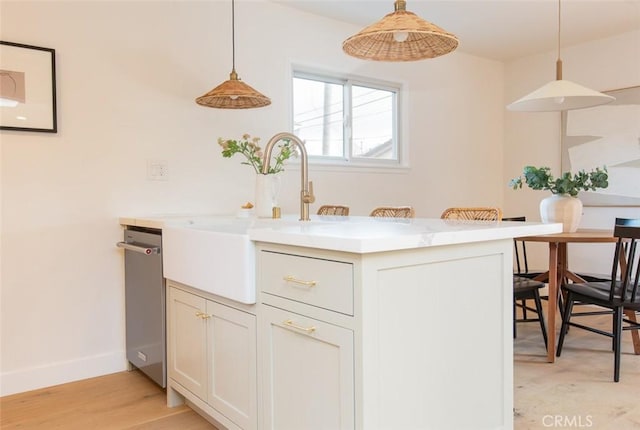 kitchen featuring sink, white cabinetry, hanging light fixtures, light hardwood / wood-style floors, and stainless steel dishwasher