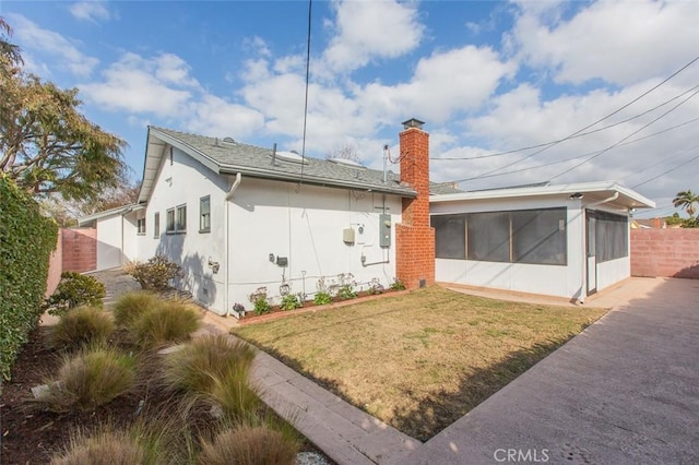 back of house featuring fence, a sunroom, a yard, stucco siding, and a chimney