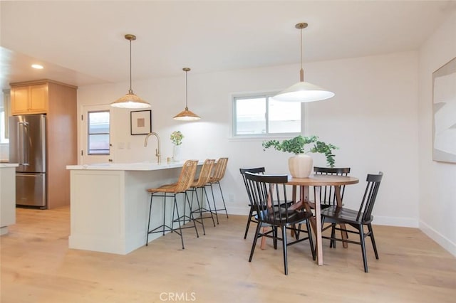 kitchen featuring a peninsula, light countertops, freestanding refrigerator, a kitchen bar, and decorative light fixtures