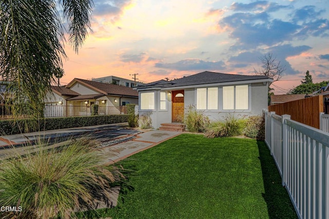 view of front of house featuring stucco siding, a yard, and a fenced backyard