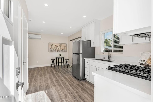 kitchen with freestanding refrigerator, light wood-style floors, white cabinets, an AC wall unit, and a sink