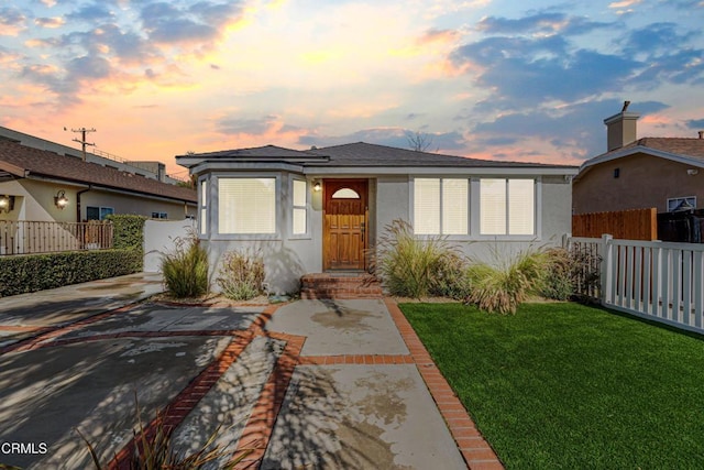 view of front of home featuring stucco siding, fence, and a front lawn
