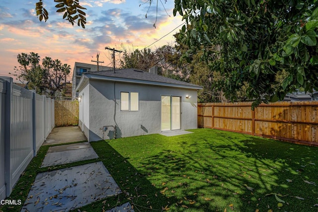 rear view of house featuring a yard, stucco siding, a fenced backyard, and roof with shingles