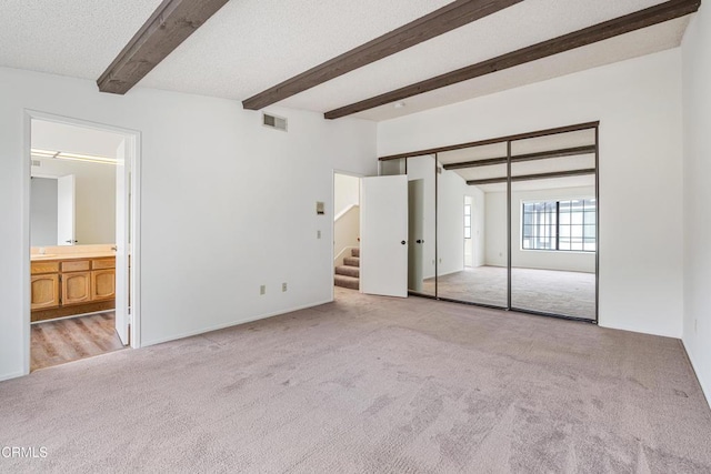 unfurnished bedroom with a closet, light carpet, a textured ceiling, and ensuite bath