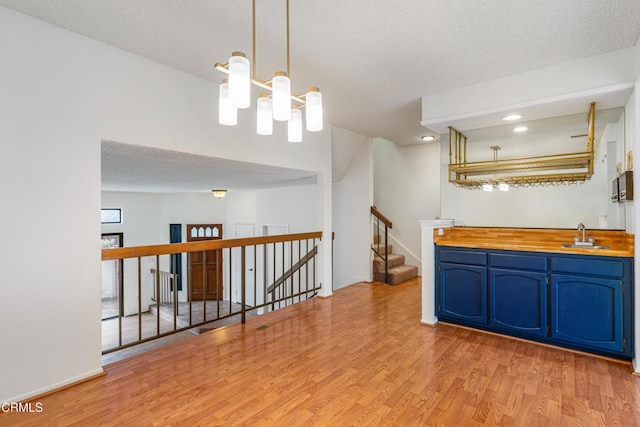 kitchen featuring blue cabinets, sink, hanging light fixtures, light wood-type flooring, and a notable chandelier