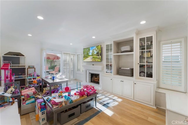 playroom with ornamental molding, a fireplace, and light wood-type flooring