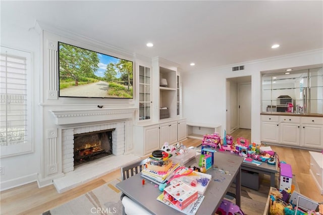 game room featuring crown molding, a fireplace, and light hardwood / wood-style flooring