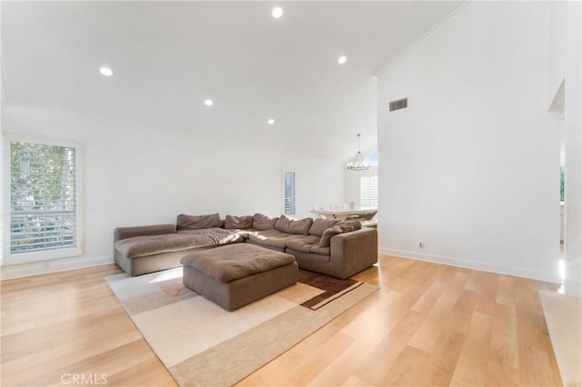 living room with crown molding, a towering ceiling, a notable chandelier, and light wood-type flooring