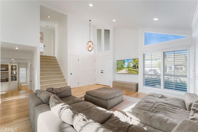 living room featuring a high ceiling, crown molding, a notable chandelier, and light hardwood / wood-style floors