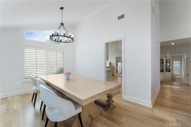 dining space featuring ornamental molding, a chandelier, light wood-type flooring, and a high ceiling