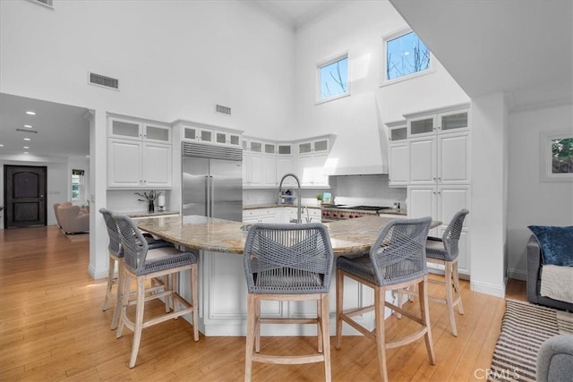 kitchen featuring a breakfast bar, light stone counters, light wood-type flooring, stainless steel built in fridge, and white cabinets