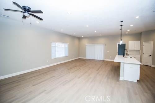 kitchen with decorative light fixtures, an island with sink, sink, white cabinets, and light hardwood / wood-style flooring