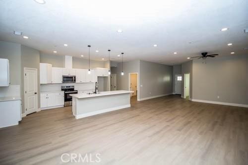 kitchen featuring light hardwood / wood-style flooring, white cabinetry, hanging light fixtures, stainless steel appliances, and an island with sink