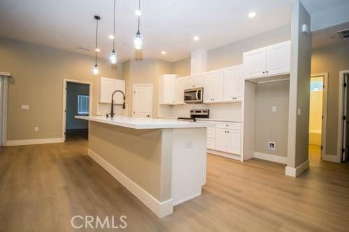 kitchen with appliances with stainless steel finishes, decorative light fixtures, an island with sink, and white cabinets