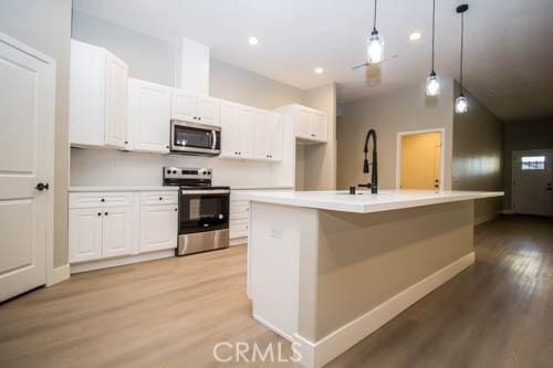 kitchen featuring decorative light fixtures, light wood-type flooring, stainless steel appliances, a kitchen island with sink, and white cabinets