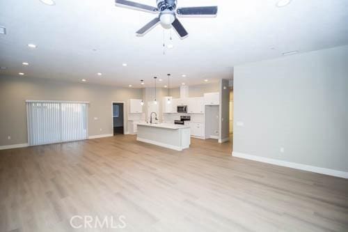 unfurnished living room with ceiling fan, sink, and light hardwood / wood-style floors