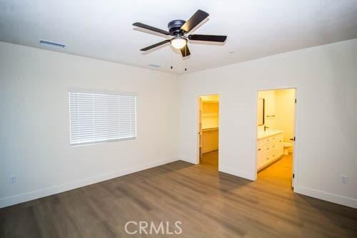 unfurnished bedroom featuring connected bathroom, a spacious closet, wood-type flooring, and a closet