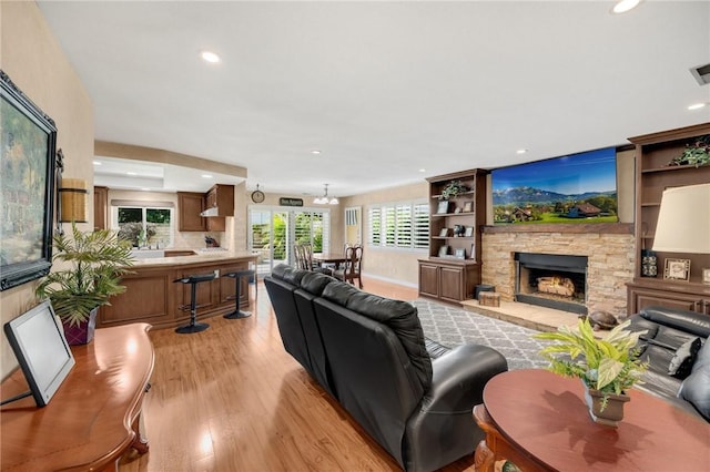 living room with a stone fireplace, light hardwood / wood-style flooring, and a notable chandelier