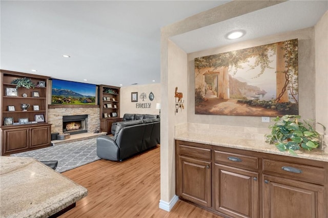 living room with a stone fireplace, built in features, and light wood-type flooring