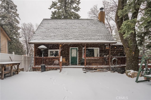 snow covered house with a shingled roof, fence, and a chimney