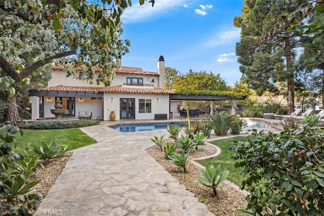 back of property featuring stucco siding, a patio, a chimney, and a tile roof