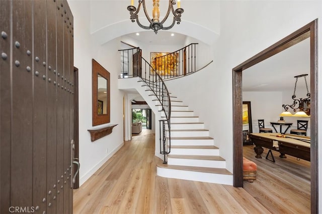 foyer entrance featuring wood finished floors, stairway, a high ceiling, pool table, and a chandelier