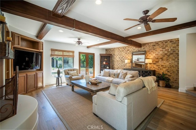 living room featuring beamed ceiling, brick wall, wood finished floors, and a ceiling fan