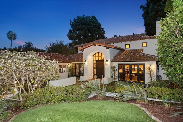 mediterranean / spanish home featuring a front yard, french doors, a tile roof, and stucco siding