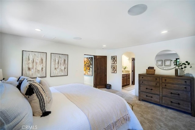 bedroom featuring arched walkways, recessed lighting, light carpet, and ensuite bathroom