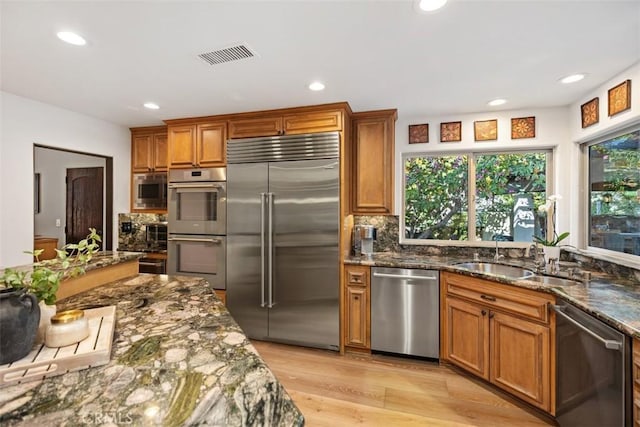 kitchen with visible vents, built in appliances, brown cabinetry, plenty of natural light, and a sink