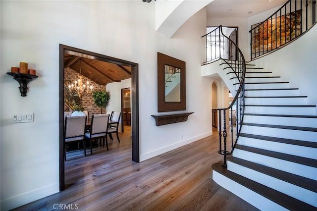 foyer with baseboards, a chandelier, stairway, wood finished floors, and arched walkways