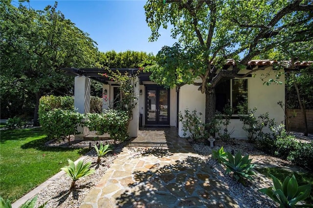 property entrance with a tile roof, french doors, a lawn, and stucco siding