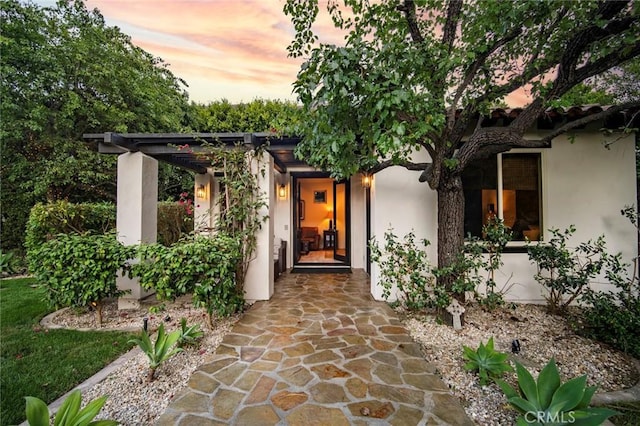 exterior entry at dusk featuring stucco siding and a pergola