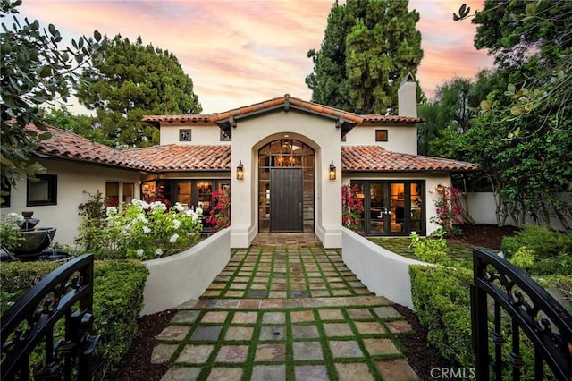 mediterranean / spanish-style house with a chimney, stucco siding, a tile roof, and fence