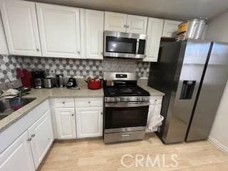 kitchen with light wood finished floors, stainless steel appliances, tasteful backsplash, light countertops, and white cabinets