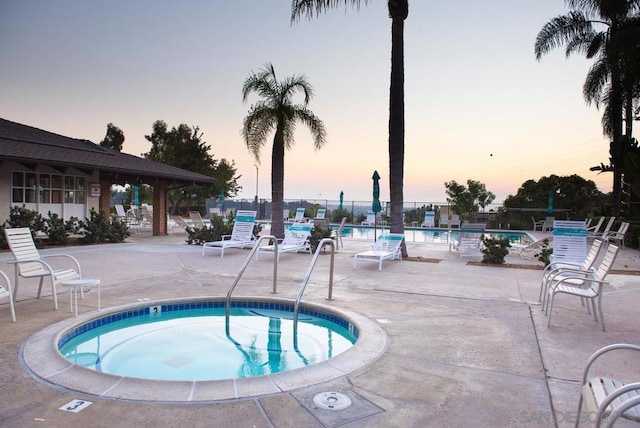 pool at dusk with a community hot tub and a patio