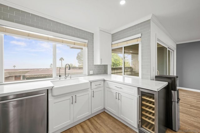 kitchen with sink, white cabinetry, ornamental molding, stainless steel dishwasher, and beverage cooler