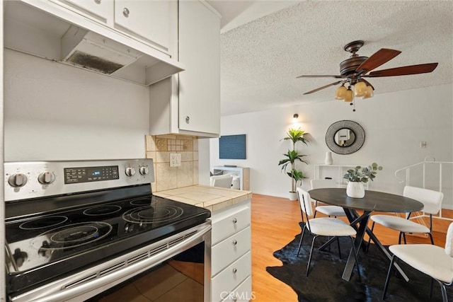 3565 Linden Ave Unit 220, Long Beach, CA 90807 - kitchen with electric range, tile countertops, white cabinetry, under cabinet range hood, and a textured ceiling