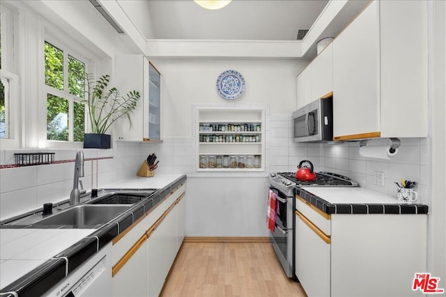 kitchen with stainless steel appliances, white cabinetry, sink, and tile countertops